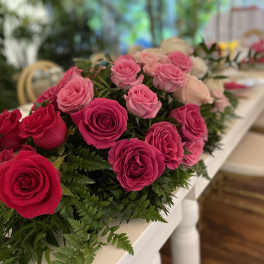 Elongated centerpiece of hot pink and light pink roses running along a white table.