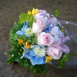 Hand-tied bouquet of pink roses, blue hydrangeas, white mums, and yellow flowers with pearl accents