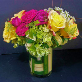Compact arrangement of yellow and hot pink roses with green hydrangeas in a striped glass vase