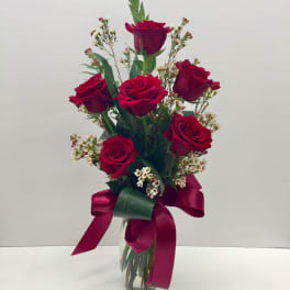 Red roses arranged in a clear glass vase with a burgundy ribbon