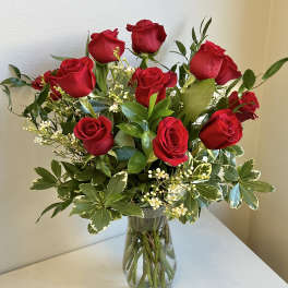 Red roses arranged in a clear glass vase with mixed greenery