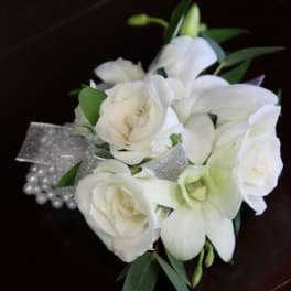 White rose and orchid wrist corsage with silver ribbon and pearls on a dark surface