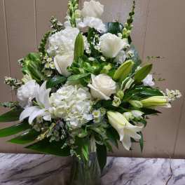White roses, lilies, and hydrangeas arranged in a glass vase
