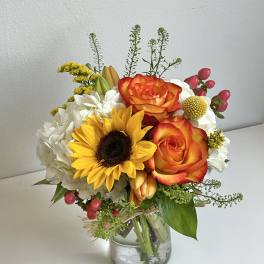 Bouquet of orange roses, a sunflower, and white hydrangeas in a glass vase