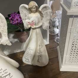 Decorative angel figurine with a heart, beside a small purple flower arrangement.