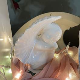 White ceramic angel figurine with pink fabric and string lights