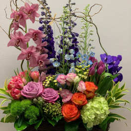 Colorful mixed flower arrangement in a woven basket with tall orchid stems