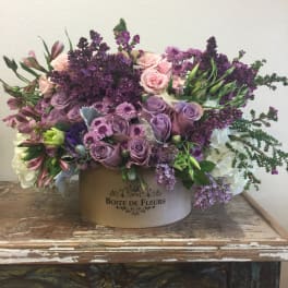 Lavender and pink floral arrangement in a round box