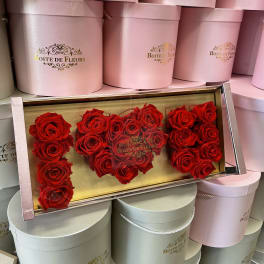 Red roses arranged in a clear rectangular box with pink round hat boxes behind