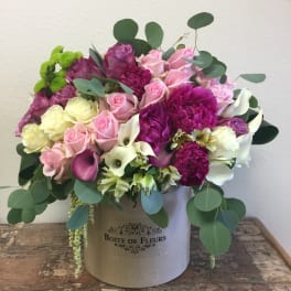 Mixed pink and white flowers arranged in a round box with greenery