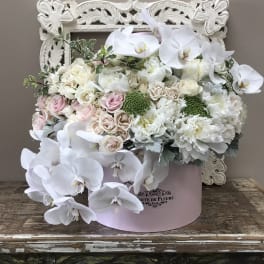 White orchids and pastel roses in a pink hatbox