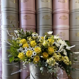 Yellow roses and white daisies arranged in a round hat box