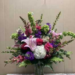Tall mixed bouquet in a clear glass vase with pink, purple, white, and green blooms