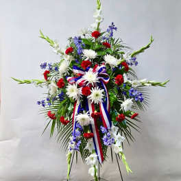Standing floral spray with white, red, and blue flowers and a ribbon bow