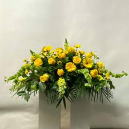 Yellow roses and daisy-like flowers arranged in a low white pedestal display.