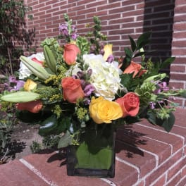 Mixed bouquet of roses, lilies, and hydrangea in a square glass vase