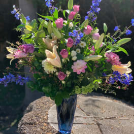 Mixed bouquet with pink roses, lilies, and blue flowers in a blue vase
