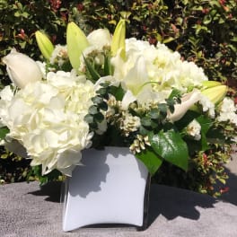 White floral arrangement in a square vase with lilies and hydrangeas