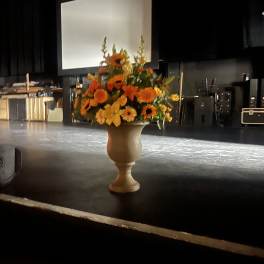 Orange and yellow floral arrangement in a pedestal vase