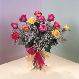 Bouquet of multicolored roses in a glass vase with a pink and gold ribbon