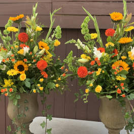 Two large floral arrangements in stone urns with orange, yellow, and white blooms