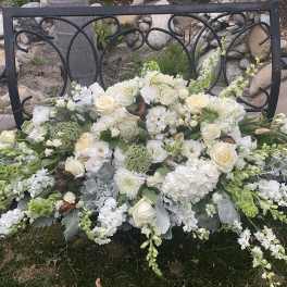 White floral arrangement with roses and mixed blooms on a black metal bench