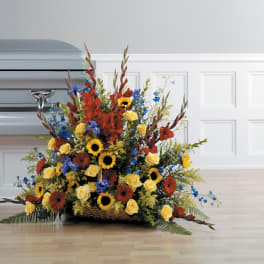 Large casket spray with yellow roses, sunflowers, red flowers, and blue accents