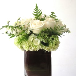 Low arrangement of white roses and green hydrangeas in a dark glass vase