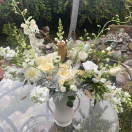 White floral arrangement in a white vase with cream roses and tall white blooms