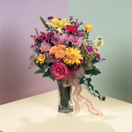 Mixed bouquet in a clear glass vase with a pink ribbon