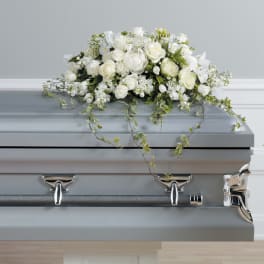 White floral casket spray with trailing greenery on a gray casket