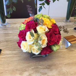 Round bouquet of multicolored roses in a low square vase