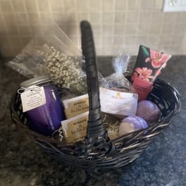 Gift basket with a purple candle, soaps, bath items, and a small dried floral bundle