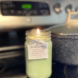 Lit green candle in a glass jar with a hanging label