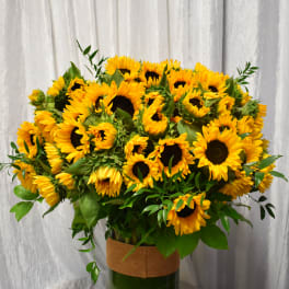 Large arrangement of yellow sunflowers in a tall clear glass vase on a table