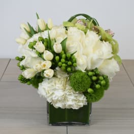White floral arrangement in a green glass vase with green accents