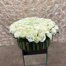 Large white rose arrangement in a glass vase on a mirrored stand