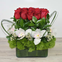 Compact arrangement of red roses, white orchids, and green dianthus in a rectangular green glass vase.