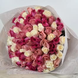 Large hand-tied bouquet of cream, blush, and hot pink roses wrapped in sheer patterned paper.