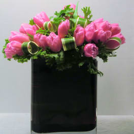 Low arrangement of pink tulips in a rectangular black glass vase with curled accents.