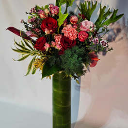 Tall arrangement of red and pink roses and carnations in a slim green glass cylinder vase