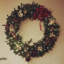 Decorated evergreen wreath with lights, pinecones, bows, and red accents