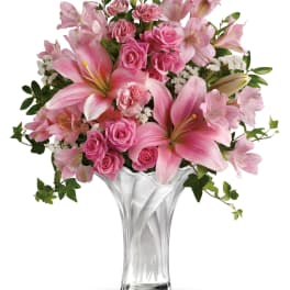 Tall clear glass vase with pink lilies, spray roses, carnations, and white filler flowers