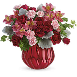 Arrangement of red roses and pink carnations with silver foliage in a shiny red vase