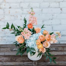 Peach roses and blue hydrangeas in a white vase