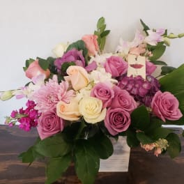 Pink and cream roses with purple blooms in a white vase