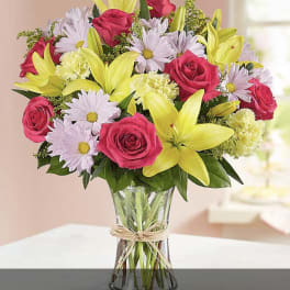 Bouquet of pink roses, yellow lilies, and pale daisies in a glass vase