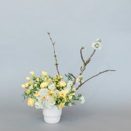 Yellow and white floral arrangement in a white vase with branching stems