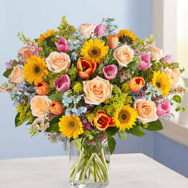 Mixed bouquet of roses, tulips, and sunflowers in a clear glass vase
