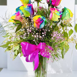 Rainbow-colored roses in a clear glass vase with a pink ribbon